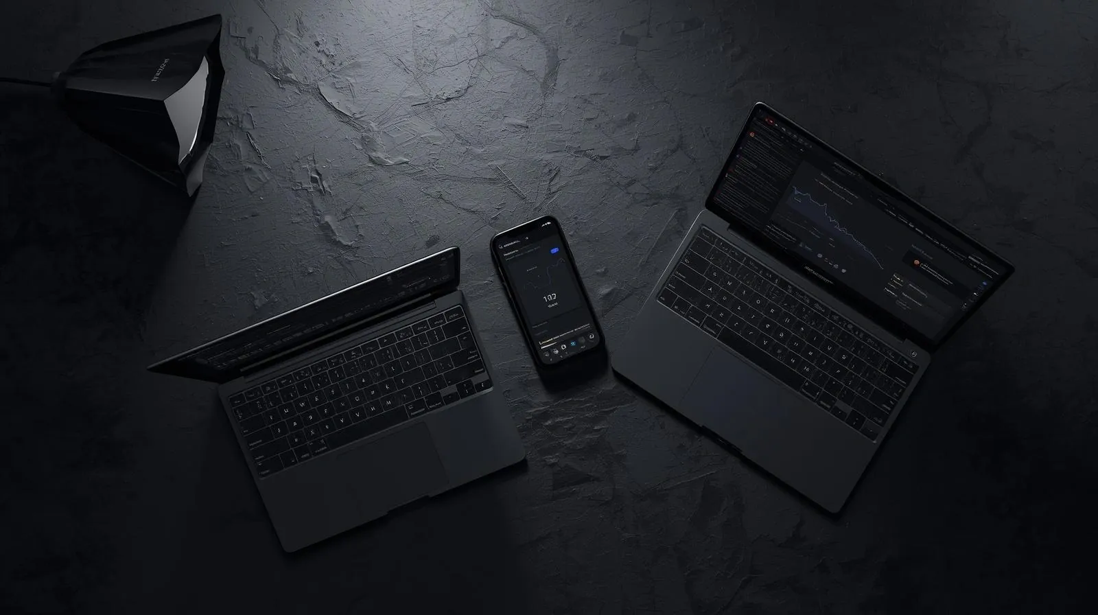 Two laptops and a phone on a dark stone desk