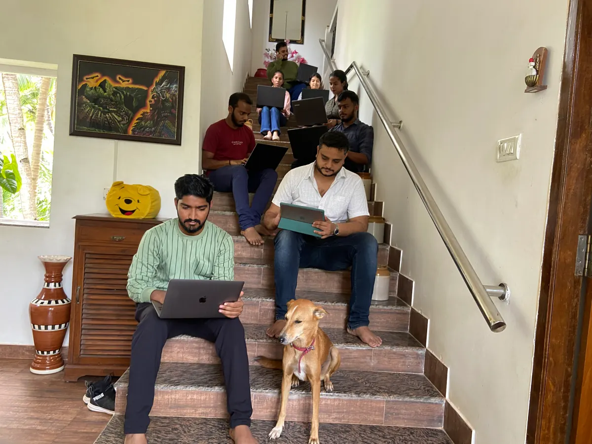 Zunderdog developers working on laptops and a tablet on a staircase, with a dog sitting in front